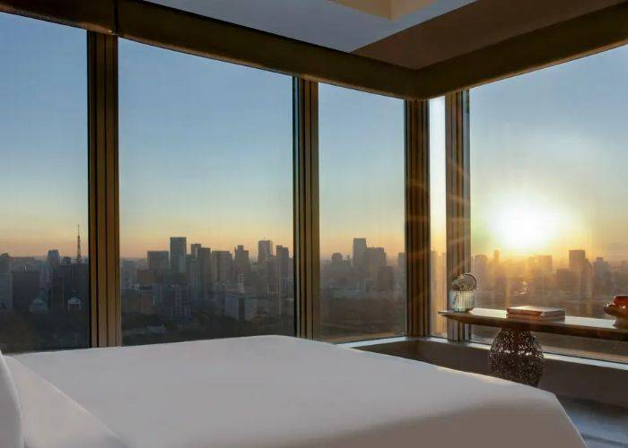 A bedroom in the Four Seasons Hotel Tokyo at Otemachi, looking out over the city of Tokyo at sunset.